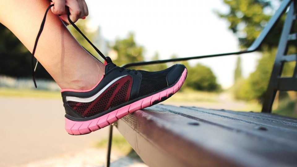 Coureuse laçant sa chaussure sur un banc au bord d'un chemin