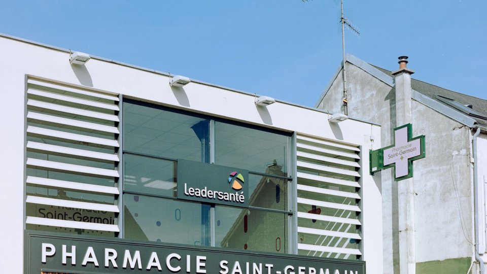 Croix verte lumineuse d'une pharmacie française sur une façade ancienne