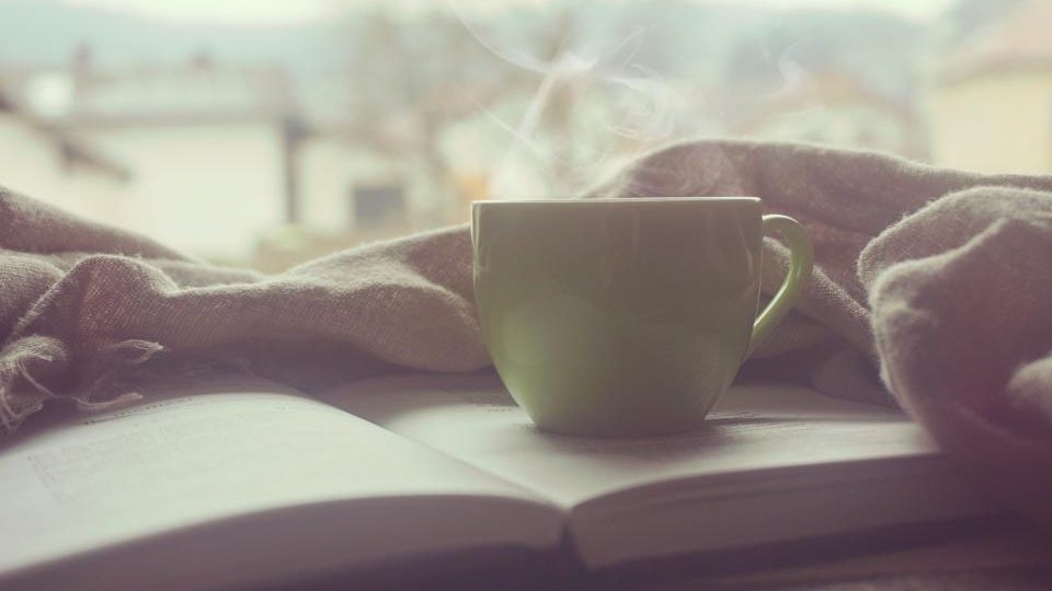 Tasse fumante sur un livre, plaid douillet près de la fenêtre